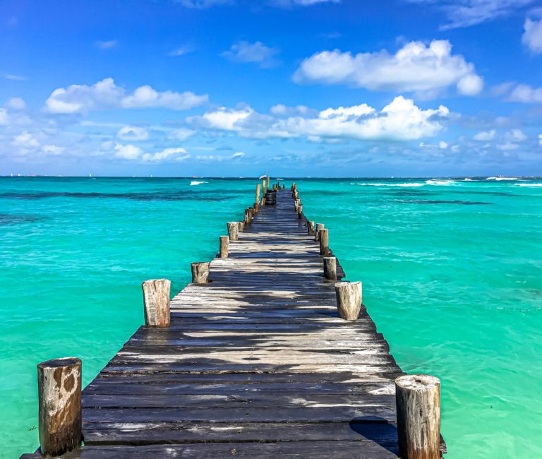 A Clear Water Beach With a Wooden Bridge